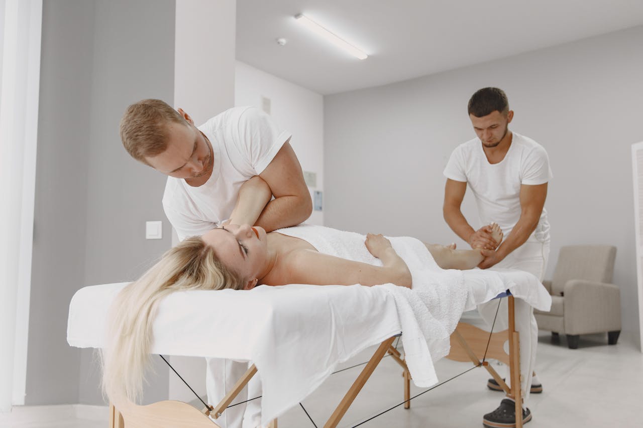 A woman receives a professional massage from two masseurs in a modern spa setting, promoting relaxation and wellness.