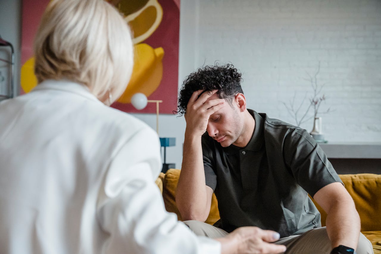 A young man in a therapy session, expressing emotions with hand on forehead.